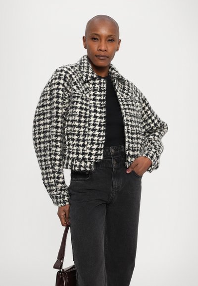 Melnbalts houndstooth žakets ar īsu dizainu, teksturētu audumu un stāvošu apkakli. Pāris ar augsto jostasvietu melnām džinsām.