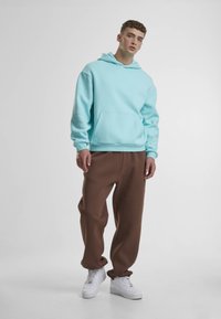 Sweat à capuche bleu clair avec une poche avant, associé à un pantalon ample marron et des baskets blanches. Design simple sans motifs.