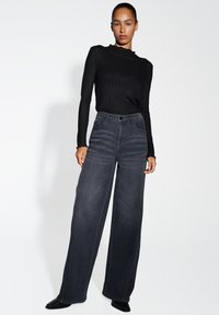 Jeans taille haute à jambes larges en denim gris foncé, avec une fermeture à bouton et des poches avant, associés à un haut noir à manches longues en maille côtelée.