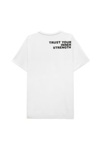 Hvid bomulds T-shirt med korte ærmer, rund hals, med teksten "BEGRIB DIN INDRE STYRKE" i sort på den øverste del af ryggen.