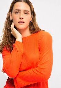 Top arancione a maniche lunghe con scollatura tonda; design aderente che mette in risalto la trama, con maniche che si estendono oltre i polsi.
