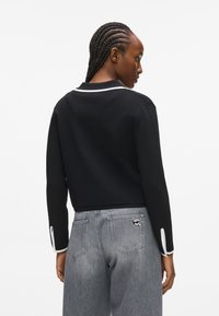 Czarny, krótkowłosy sweter z białym kołnierzykiem i akcentami na rękawach, o gładkiej fakturze. Połączony z jasnoszarymi dżinsami z logo.