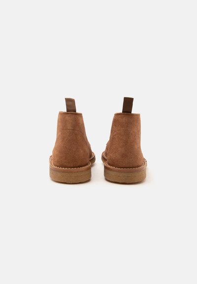 Paire de bottines en daim marron vues de dos, avec languettes de traction et semelles en caoutchouc cousues.