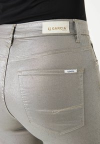 Zilveren metallic jeans met een gladde textuur en een aansluitend ontwerp. Heeft achterzakken en een merklabel op de tailleband.