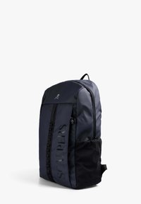 Mochila de un oscuro color azul marino con acentos negros, de construcción de tela, con un zipper central, un bolsillo de malla lateral y el logotipo "SCALPERS" exhibido de manera prominente.