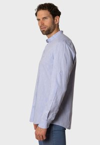 Camisa de manga larga azul claro en una tela texturizada, que presenta un cuello abotonado y cierres de botones en la parte delantera y en los puños.