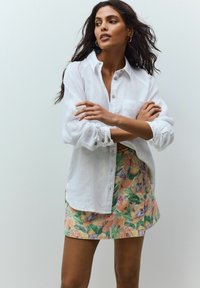 Vit linneskjorta med knappar och uppvikt ärm, tillsammans med en blommig minikjol i pastellfärger med tulpanmönster och gröna detaljer.