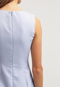 Jasnoniebieski bezrękawnik z teksturowanej tkaniny z diamentowym wzorem, detal z zamkiem z tyłu oraz dopasowana sylwetka.