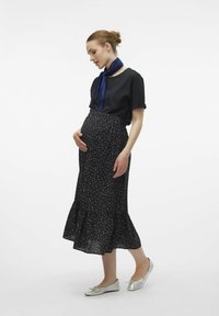 Jupe maxi noire à pois avec ourlet volanté, portée avec un t-shirt noir et une écharpe bleue marine, associée à des ballerines argentées.