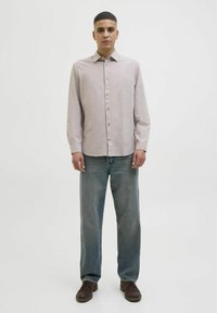 Camisa de botón gris claro con mangas largas, combinada con jeans azules de corte holgado. Unos zapatos marrones oscuros completan el atuendo. Diseño sencillo, textura suave.