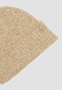 Beanie tricoté beige fabriqué dans un matériau doux et texturé. Présente un revers replié et un petit logo en relief sur le côté.