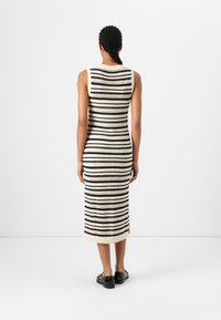 Robe maxi en tricot avec des rayures verticales noires et crème, dotée d'un design sans manches et d'accents en tissage ouvert, terminée par un ourlet côtelé.