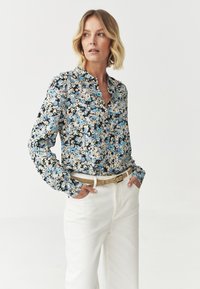 Cămașă cu imprimeu floral, cu butoni, având un model negru, albastru și crem, cu mâneci lungi și guler, asociată cu pantaloni albi, cu talie înaltă.