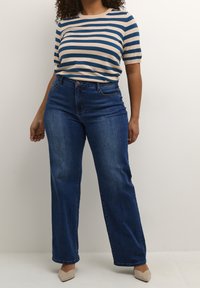 Stribet kortærmet top i beige og blå, parret med højtaljede, brede mørk denim jeans. Lyse hæle fuldender looket.