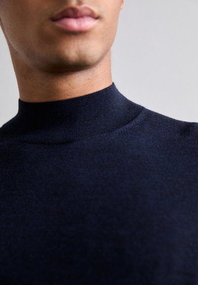 Pull à col montant bleu marine en tissu tricoté doux ; présente une texture lisse et des coutures minimales pour une finition propre.