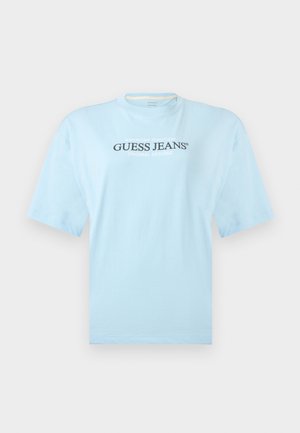 Svetlomodré tričko s krátkym rukávom s nápisom „GUESS JEANS“ a menšími frázami „AMERICAN TRADITION“ a „ORIGINAL DESIGNS“ v strede prednej strany.