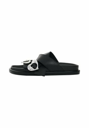 Black slide sandal with two wide crisscross straps and large silver heart-shaped buckles on each strap.