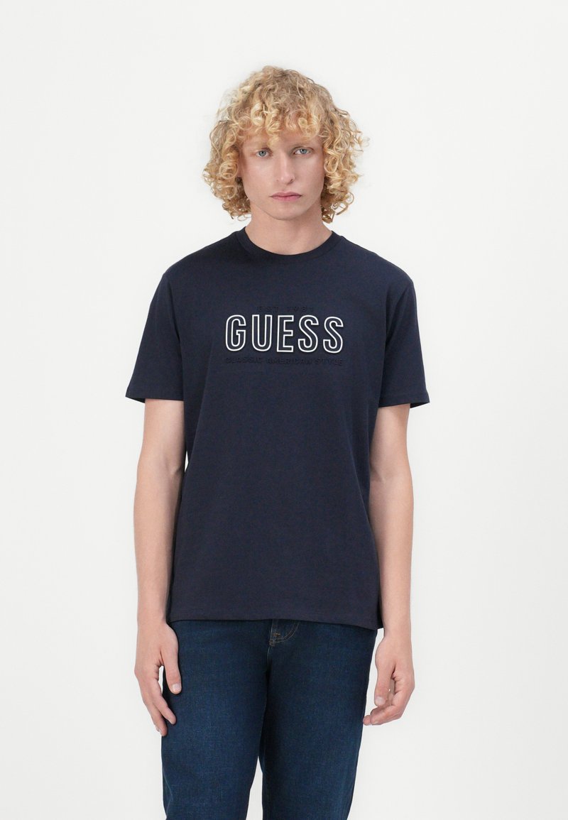 Navy blue cotton T-shirt featuring a round neckline and short sleeves, with the "GUESS" logo in white text across the chest.