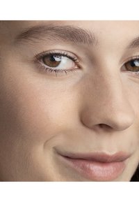 Gros plan sur un visage montrant une texture de peau lisse, des yeux marron clair et des lèvres naturelles. Le sourcil est bien entretenu, mettant en valeur la forme de l'œil.
