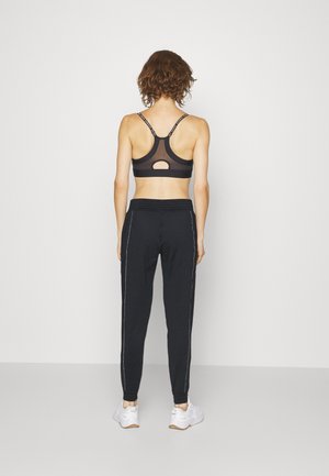 Sort sports-bh med mesh-detaljer og krydsede stropper, parret med sorte tapered sweatpants med sidepiping og elastisk talje.