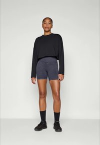 Zwarte cropped lange mouwen top gecombineerd met donkergrijze, strakke shorts en zwarte sportieve schoenen. Glad materiaal, minimalistisch ontwerp.