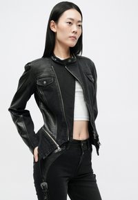 Μαύρη δερμάτινη μοτοσικλετιστική τζάκετ με φερμουάρ μπροστά, κουμπωτό γιακά και πλαινές τσέπες, σε συνδυασμό με μαύρα τζιν με ψηλή μέση και υφές.