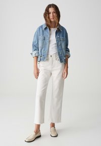 Leren spijkerjack in lichtblauw met grote borstzakken, gecombineerd met een witte t-shirt en witte hoog-waisted, cropped broeken. Beige loafers.