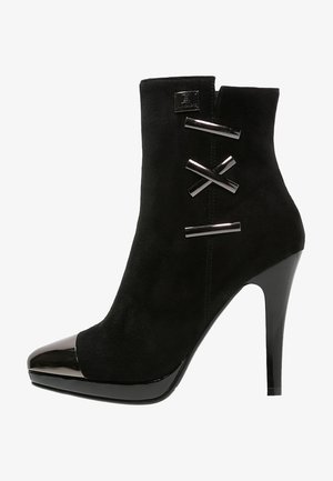 Sort ankelstøvle i ruskind med blank sort tåhætte og hæl, dekoreret med tre skinnende vandrette metalstænger på siden.