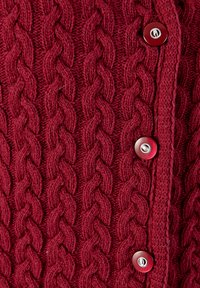 Pull en tricot bordeaux avec un motif de torsades, doté de cinq boutons ronds contrastants sur le devant. Tissu texturé avec des points visibles.