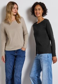 Långärmade skjortor i beige och svart bomull, kombinerade med blå denimjeans. Den beige skjortan har en avslappnad passform och rund halsringning.