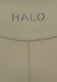 Gros plan sur un tissu beige avec des coutures noires cousues et le mot « HALO » imprimé en lettres majuscules noires.