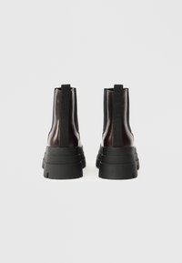 Μαύρα μποτάκια με φαρδύ τακούνι και ανατομικά άκρα, κατασκευασμένα από ματ δέρμα, με ελαστικές πλευρικές επενδύσεις και κωνικές σόλες από καουτσούκ, που διαθέτουν θηλιά στο πίσω μέρος.