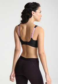 Svart sports-bh med justerbare stropper, med en strukturert bakside og rosa detaljer. Båret med mørke leggins som fremhever en slank design.