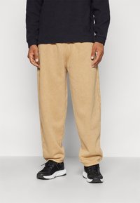 Beige fleece joggingbroek met een relaxte pasvorm; voorzien van een elastische tailleband en boorden, gecombineerd met zwarte sportschoenen.