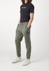 Svart bomull T-shirt med "Calvin Klein" logotyp, i kombination med olivgröna joggers med elastisk midja och sidofickor.