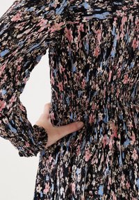 Sukienka w kwiatowy wzór w kolorach czarnym, różowym i niebieskim. Posiada długie rękawy, marszczoną talię oraz fakturowaną tkaninę z marszczonym detalem.