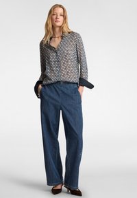 Camicia a maniche lunghe con bottoni in un motivo geometrico blu e beige, abbinata a pantaloni di jeans larghi a vita alta e calzature marroni.
