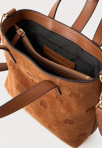 Καφέ σουέτ τσάντα χειρός με δερμάτινες λεπτομέρειες, διαθέτει εσωτερική τσέπη με φερμουάρ και ανάγλυφο λογότυπο. Δύο μακριές χερούλια για εύκολη μεταφορά.