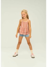 Rosa och vit randig ärmlös topp med volangdesign, tillsammans med denimshorts. Modellen bär vita låga sneakers och beige strumpor.