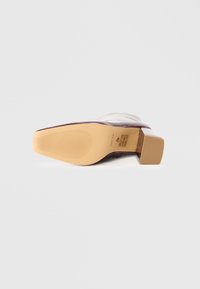 Zapato de tacón con parte superior de charol burdeos, puntera cuadrada y suela de goma beige con un patrón de agarre texturizado.