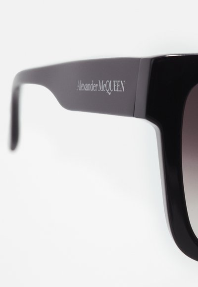 Ochelari de soare negri cu o ramă groasă, pătrată, având lentile degradate. Brațul este embosat cu "Alexander McQueen" în argintiu.