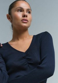 Granatowy prążkowany longsleeve z dekoltem w kształcie litery V i marszczeniem na środku. Gładka tekstura i dopasowany krój, idealny do codziennych stylizacji.