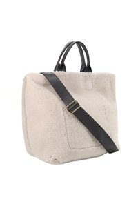 Sac fourre-tout en fausse fourrure beige avec des poignées en cuir noir et une sangle amovible, présentant une forme rectangulaire et des détails de couture visibles.