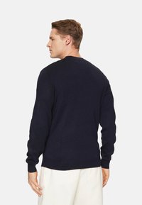 Suéter de punto azul marino con cuello redondo, mangas largas y puños acanalados. Textura suave y corte clásico. La vista trasera muestra líneas limpias.