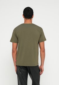 Λαδί κοντομάνικο μπλουζάκι από βαμβάκι, με στρογγυλή λαιμόκοψη και μικρή ετικέτα λογότυπου κοντά στο τελείωμα. Ομαλή, ελαφριά υφή.