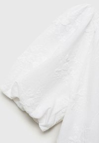 Vit blus med puffärmar, blommönster, strukturerad tyg och elastiska ärmslut. Slätt och lätt material.