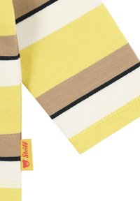 Geel, bruin en wit gestreepte stof met zwarte accenten. Bevat een rood 'Steiff' label. Zachte gebreide textuur. Korte mouwen zichtbaar.