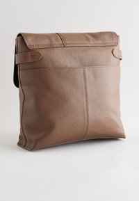 Sac bandoulière en cuir marron texturé avec un rabat à pli et des détails de sangle cousus sur un fond clair uni.