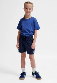 Blå bomullst-shirt, marinblå shorts med dragsko, vita sportstrumpor, mörka sneakers med gröna detaljer och logotypdetaljer på kläderna.
