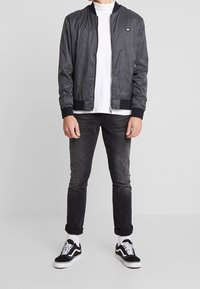 Svart bomberjacka med ribbat krage och mudd, bärs över en vit t-shirt. Kombineras med urblekta svarta jeans och svarta sneakers med vita detaljer.